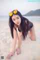 A woman in a black bathing suit and sunglasses on a beach.