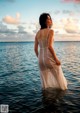 A woman in a white dress standing in the ocean.