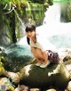 A woman sitting on a rock in front of a waterfall.