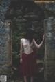 A naked woman in a red dress standing in front of a stone wall.