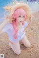 A woman with pink hair wearing a straw hat on the beach.