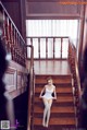 A woman in a white bodysuit sitting on a wooden staircase.