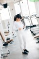 A woman in a white top and white leggings in a gym.