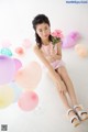 A young girl sitting on the floor holding a bunch of balloons.