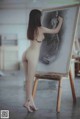 A naked woman standing in front of a drawing on a easel.