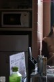 A shirtless woman sitting in front of a microwave in a kitchen.